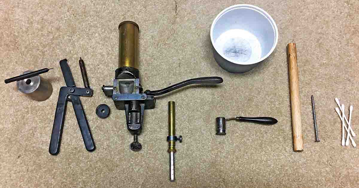 Left to right: punch and handheld decappers, shell holder, powder measure, shot container and dipper, wood dowel, sharp nail and cotton swabs.